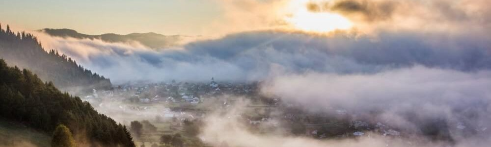 Photo of Bucovina landscape in the morning, depicting a valley covered in fog.